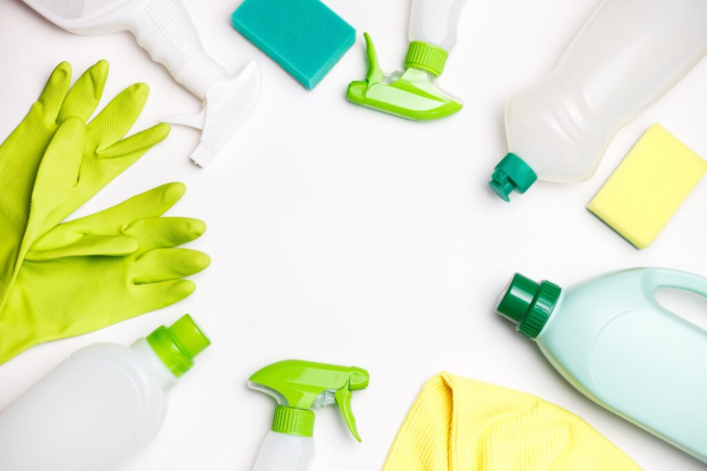 Bouteilles avec agent de nettoyage écologique, éponges de nettoyage vertes et gants posé sur une table blanche