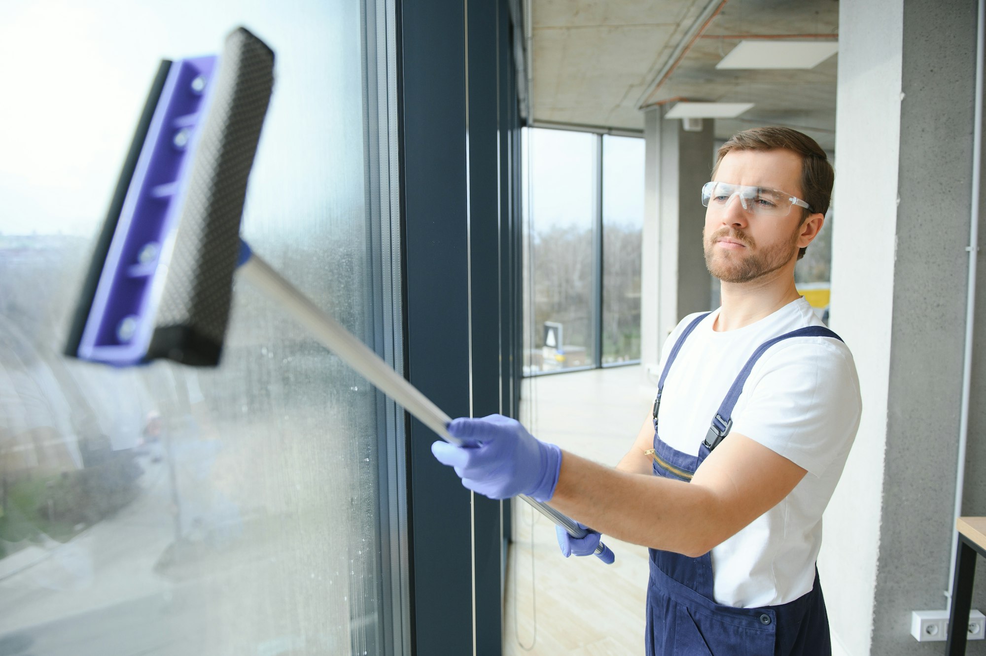 Male professional cleaning service worker in overalls cleans the windows and shop windows